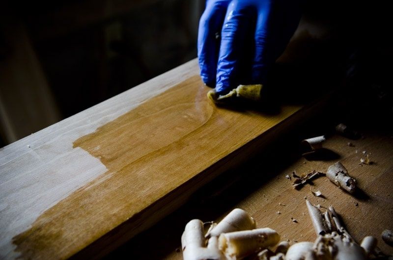 Blåhandskad hand oljar in en träskiva med en trasa